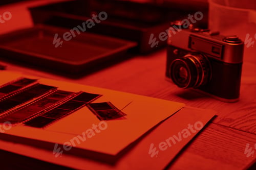 Preview: A table with analog camera and film strips under the glow of red light in darkroom, timeless