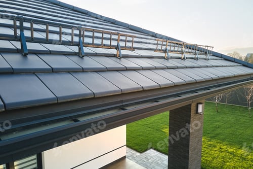 Preview: Closeup snow guard for safety in winter on house roof top covered with ceramic shingles.