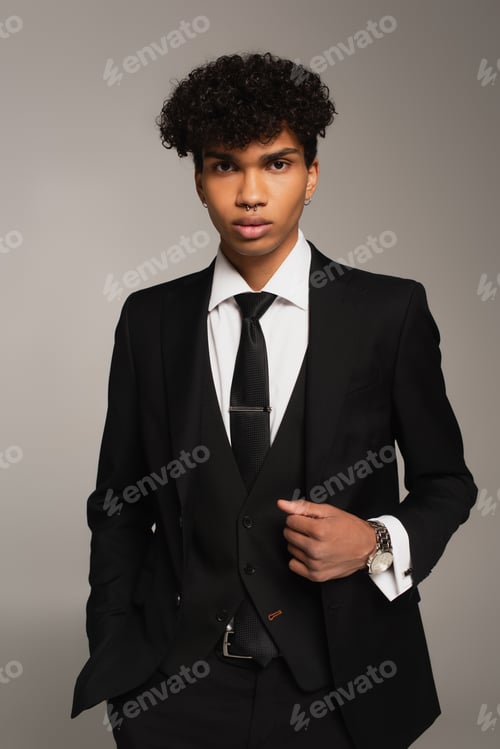 Preview: young african american man in black three-piece suit holding hand in pocket isolated on grey