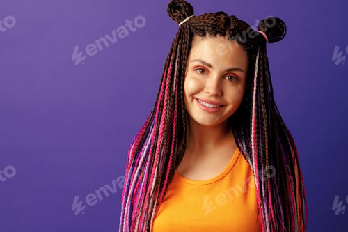 Preview: Smiling positive young woman with colorful african braids on purple background