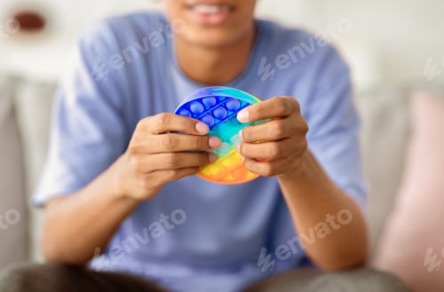 Preview: Closeup view of African American teenager playing with antistress POP IT toy at home