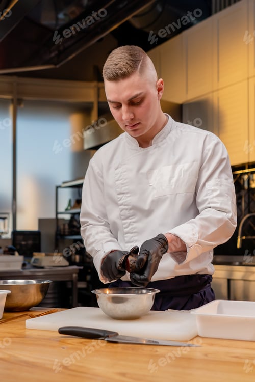 Preview: assistant chef in the kitchen in white jacket cuts beets in his hands over the table