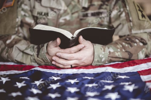 Preview: American soldier mourning and praying with the Bible in his hands and the American flag