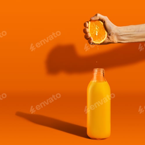 Preview: Hand squeezing orange juice in bottle on bright background
