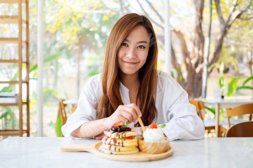 Preview: woman eating ice cream and a mixed berries pancakes with whipped cream by wooden spoon