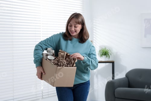 Preview: Recycling. Smiling woman holding cardboard box with different waste paper indoors