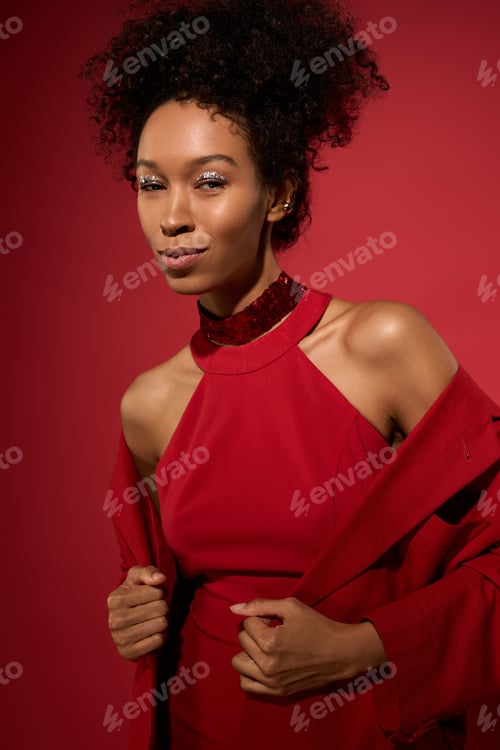 Preview: Captivating young woman in vibrant red outfit exuding confidence and charm in a studio setting
