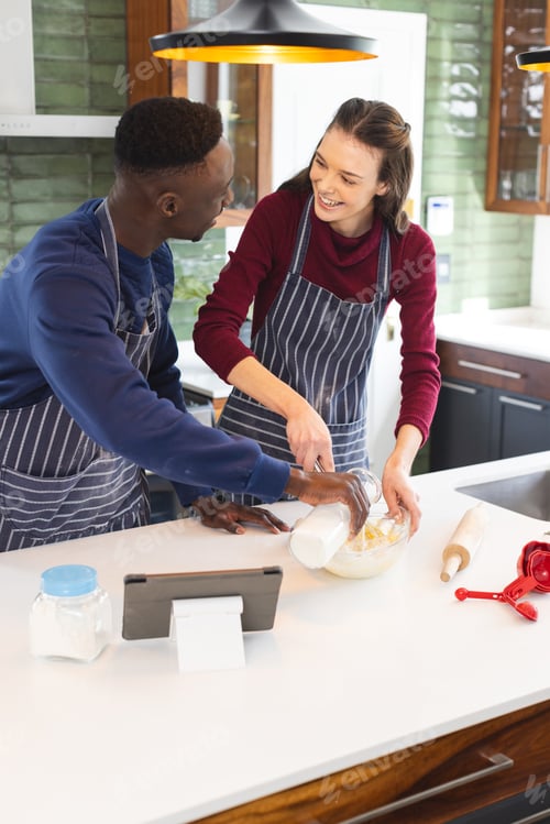Preview: Happy diverse couple baking together in kitchen, using tablet at home