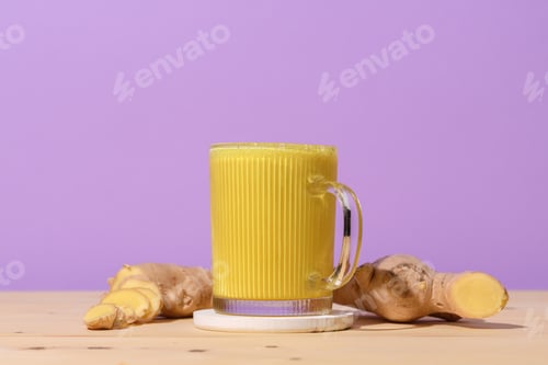 Preview: Glass mug filled with vibrant golden turmeric latte on wooden table, fresh ginger roots nearby