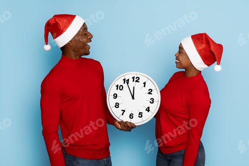 Preview: Couple celebrating New Year's Eve holding a clock wearing Santa hats