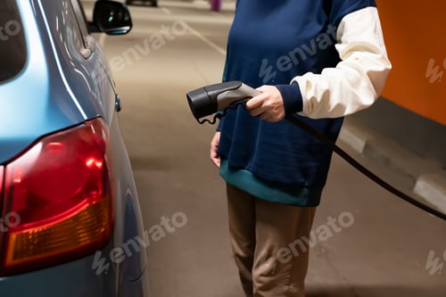 Preview: Woman hand charging a electric car at the electric gas station with sunlight.Smiling woman operating