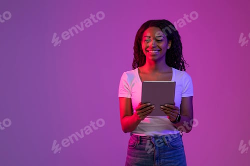 Preview: Smiling Black Woman With Digital Tablet In Hands Standing In Neon Light
