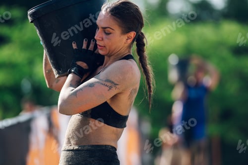 Preview: Fit woman carrying heavy barrel on her shoulder during an obstacle course race