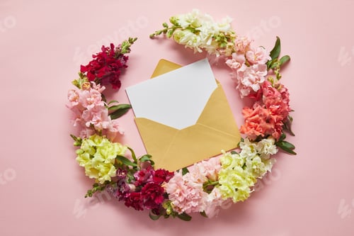 Preview: top view of beautiful tender flowers and blank card in envelope on pink