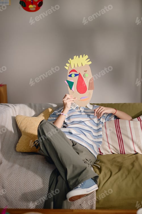 Preview: Generation Alpha Child Relaxing on Sofa While Holding Abstract Paper Mask