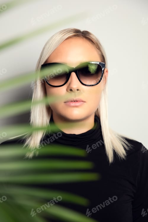 Preview: Beautiful woman with sunglasses hiding behind tropical palm leaves