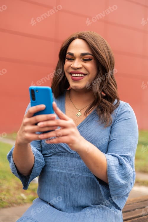 Preview: Trans woman using in blue dress using cellphone over a red background