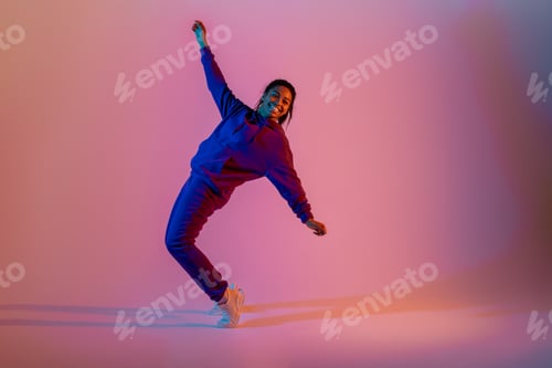 Preview: Sport dancing. Athletic and graceful black lady in sportwear dancing on pink neon background, full