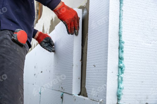 Preview: Construction worker installing styrofoam insulation sheets on house facade wall