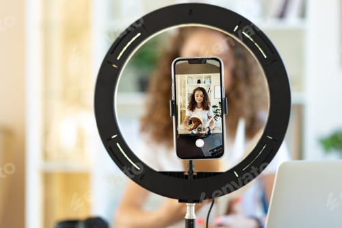 Preview: Young curly female blogger recording video at table at home