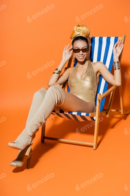 Preview: Full length of fashionable african american model in swimsuit and sunglasses waving hand on deck