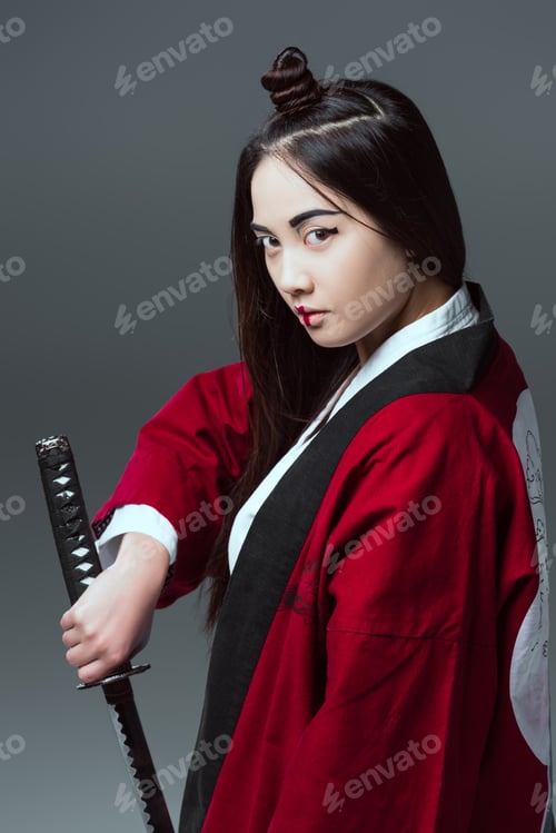 Preview: young asian woman in kimono holding katana and looking at camera isolated on grey