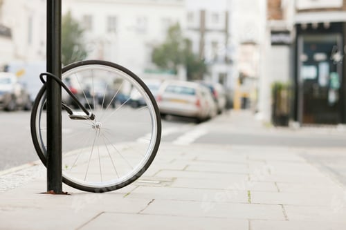 Preview: A lonely bicycle wheel locked to a post on a city street.