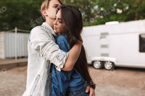 Preview: Romantic young couple in love hugging spending time in park with gray trailer on background