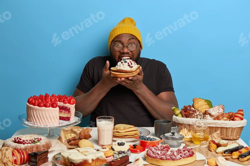 Preview: Unhealthy nutrition and sugar addiction concept. Dark skinned guy devours tasty creamy pancakes, eat
