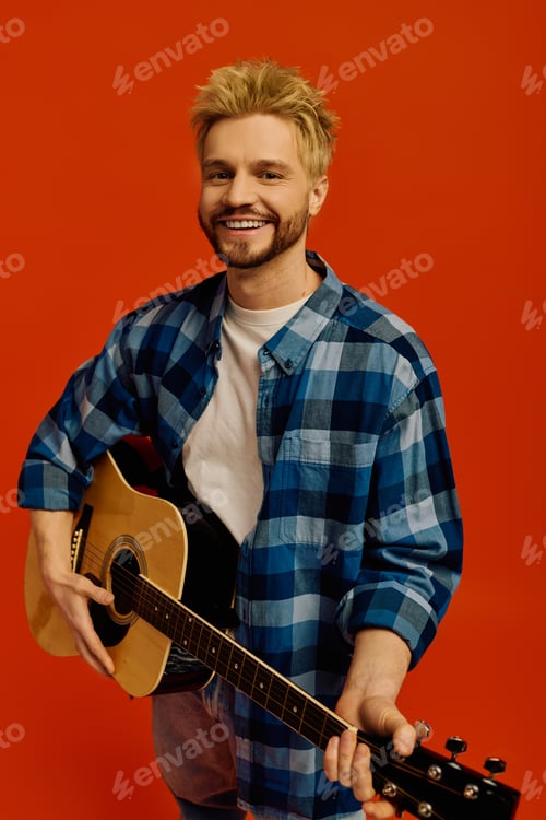Preview: Handsome young man with guitar smiles against bright orange backdrop in a lively atmosphere