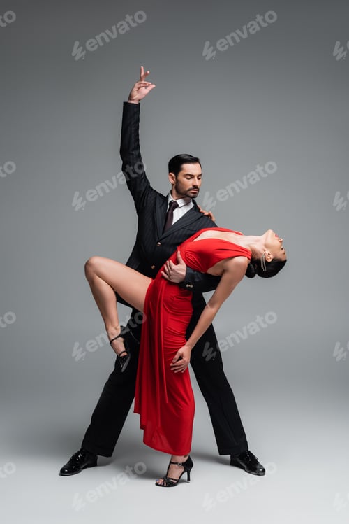 Preview: Elegant man posing while performing tango choreography with partner on grey background