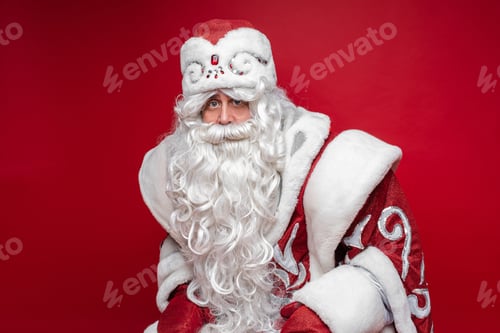 Preview: portrait of father frost in long warm coat, red gloves and a hat sits and looks to the camera