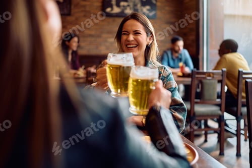 Preview: Cheerful women toasting while drinking beer in a pub.