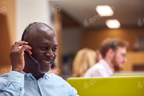 Preview: Mature Businessman Wearing Phone Headset Talking To Caller In Busy Customer Services Centre