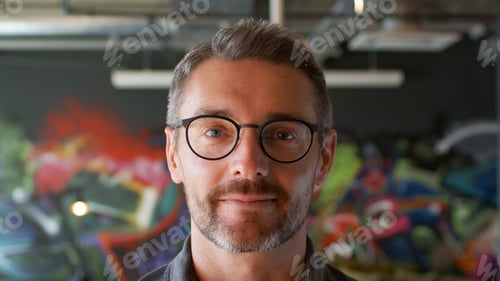 Preview: Portrait Of Mature Man Wearing Glasses In Urban Setting With Graffiti Covered Wall Behind