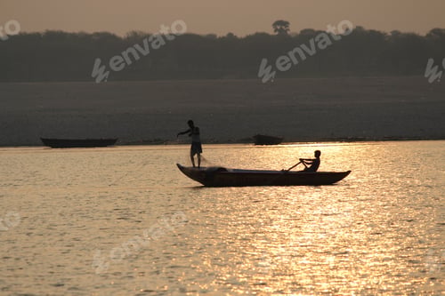 Preview: Silhouette of a boat on which one person is sailing and the second one is catching fish at sunset