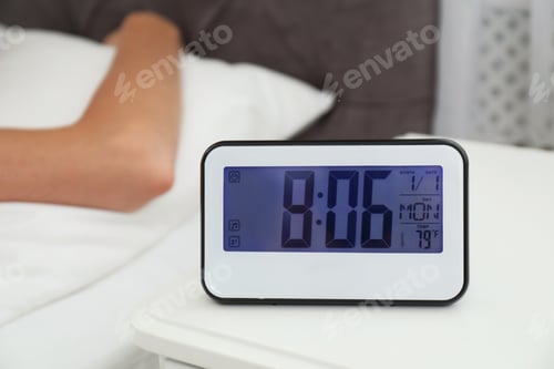 Preview: Digital alarm clock and blurred woman on background. Time of day