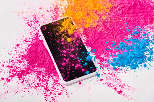 Preview: top view of smartphone and explosion of multicolored holi powder on white background