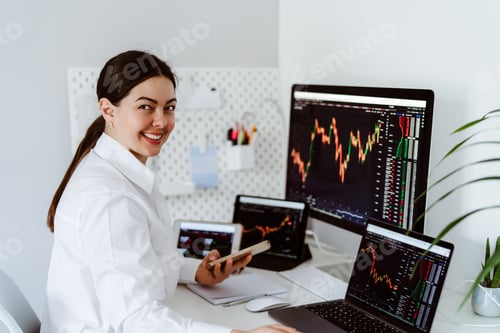 Preview: Young girl cryptocurrency trader sitting at desk with multiple screens looking at camera