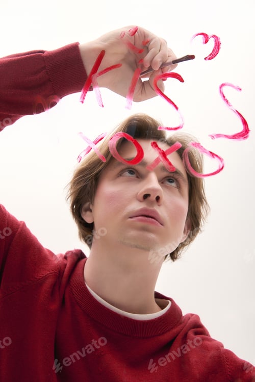 Preview: Stylish young man creating a heartfelt message on a window with vivid colors in a bright room