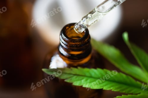 Preview: Cosmetic pipette with cannabis oil dripping into a pharmaceutical bottle near a marijuana leaf