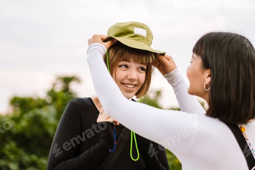 Preview: Multiracial two women wearing hat and smiling while walking together