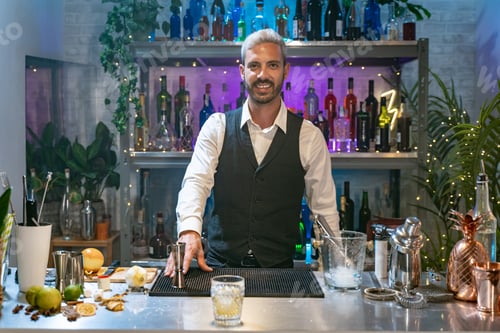 Preview: Barman portrait in a white shirt and black apron smiling looking to camera at party in nightclub