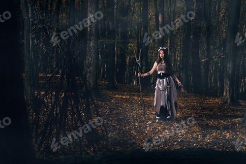 Preview: Young female with long hair and face paint in a witch costume casting a spell in a forest