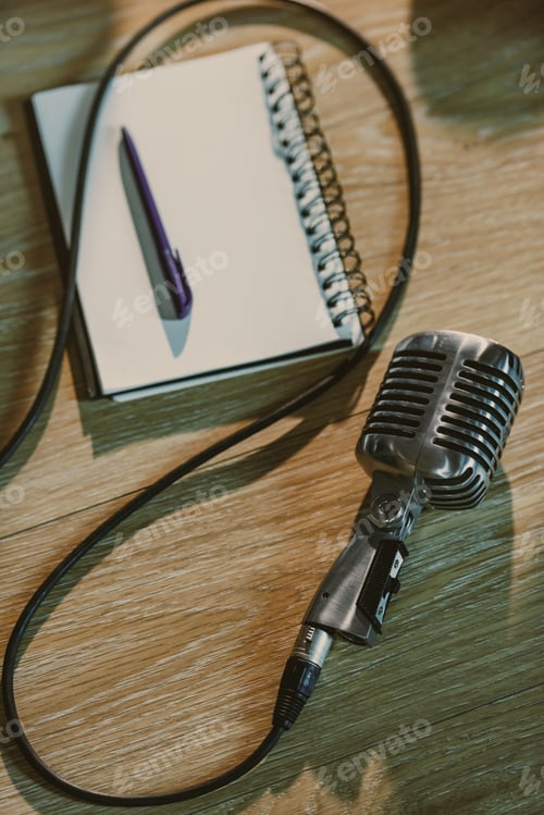 Preview: top view of wired retro microphone lying on wooden table with blank notebook