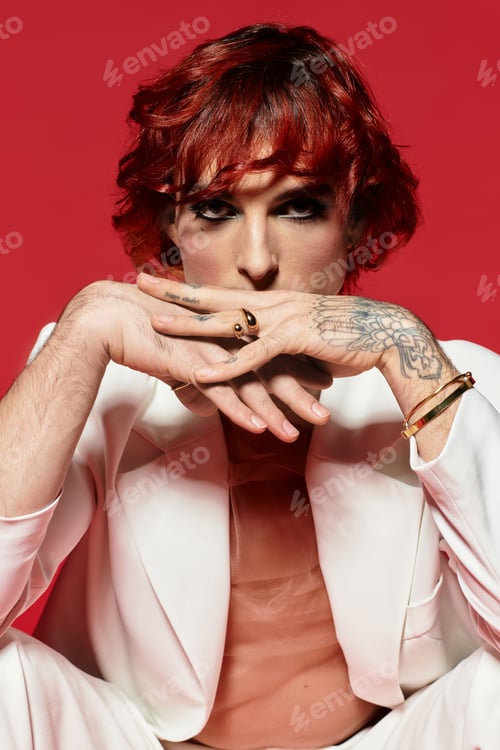 Preview: A handsome young man with vibrant red hair sits thoughtfully against a bold red backdrop.