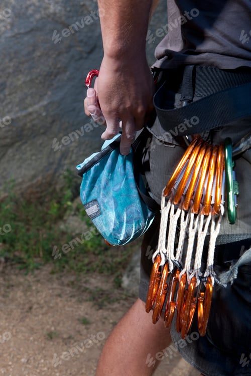 Preview: Cropped shot of young male climber attaching carabiners to belt