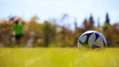 Preview: Soccer ball in field on the right side ready to be kicked. Blurred players and nature background.