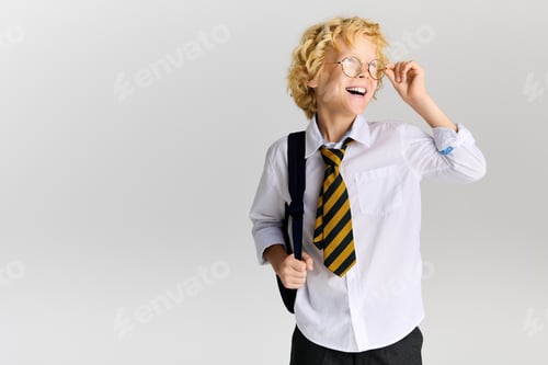 Visualização: Wavy-haired blonde boy in school uniform smiles brightly in studio setting