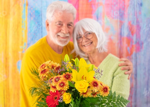 Preview: Blurred senior couple isolated on colorful background holding a flower bouquet